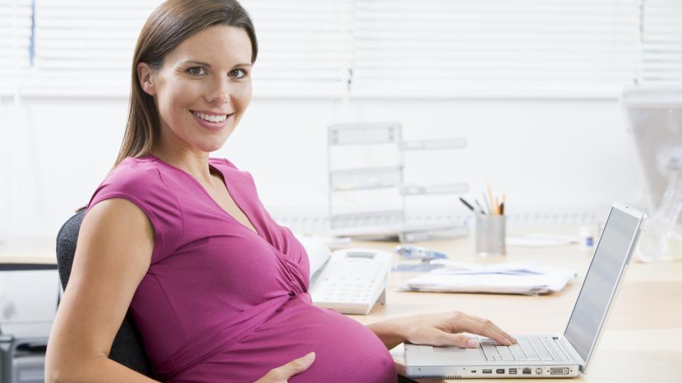 Eine schwangere Frau sitzt an einem Laptop