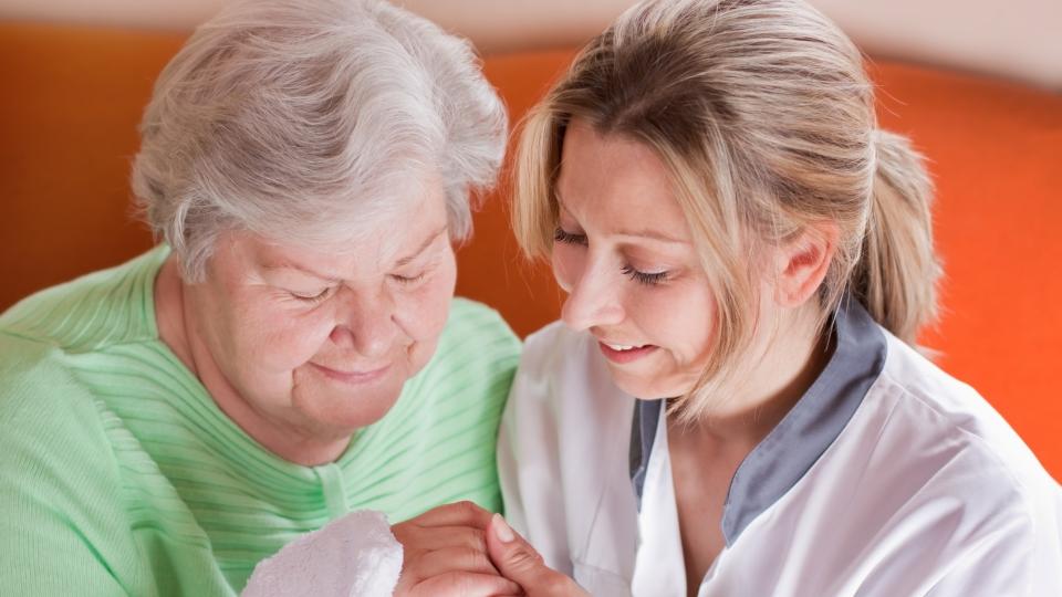 Eine Pflegekraft hält die Hand einer älteren Dame 