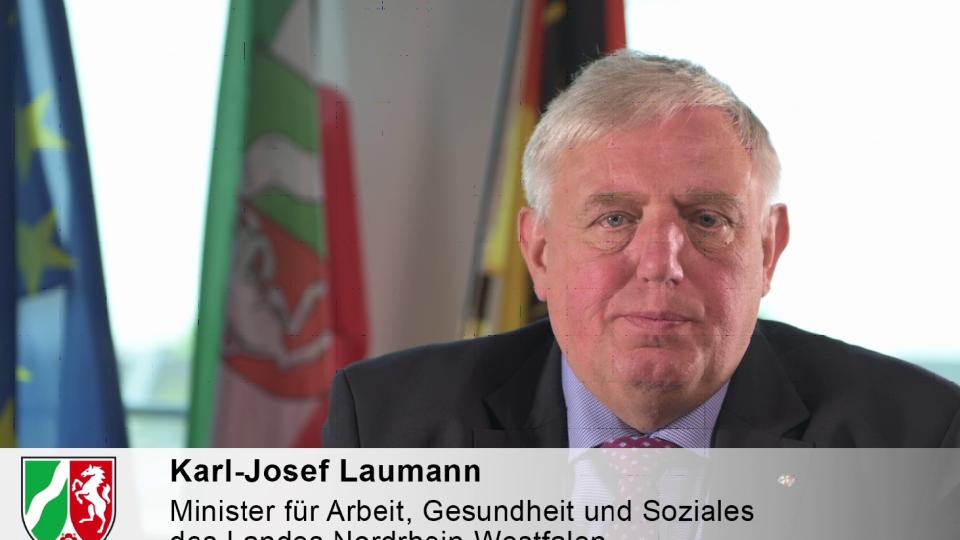 Minister Laumann vor den Fahnen von EU, Deutschland und NRW