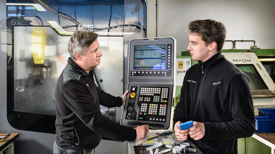 Mann zeigt einem anderen Mann wie eine CNC-gesteuerte Werkzeugmaschine funktioniert