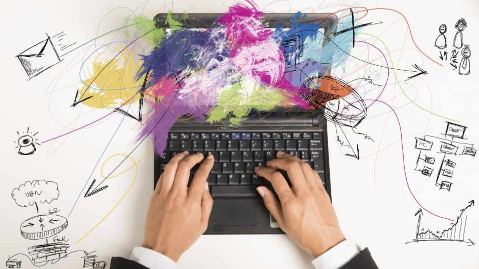 Foto: Multitasking. Businessfrau arbeitet mit Laptop, daneben Zeichnungen Jobaufgaben