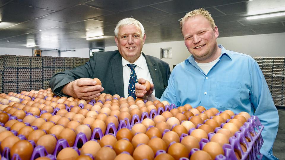 Arbeitsminister und Geschäftsführer der Owi-Ei-Erzeugergemeinschaft stehenvor einer "Eier-Loader-Maschine"