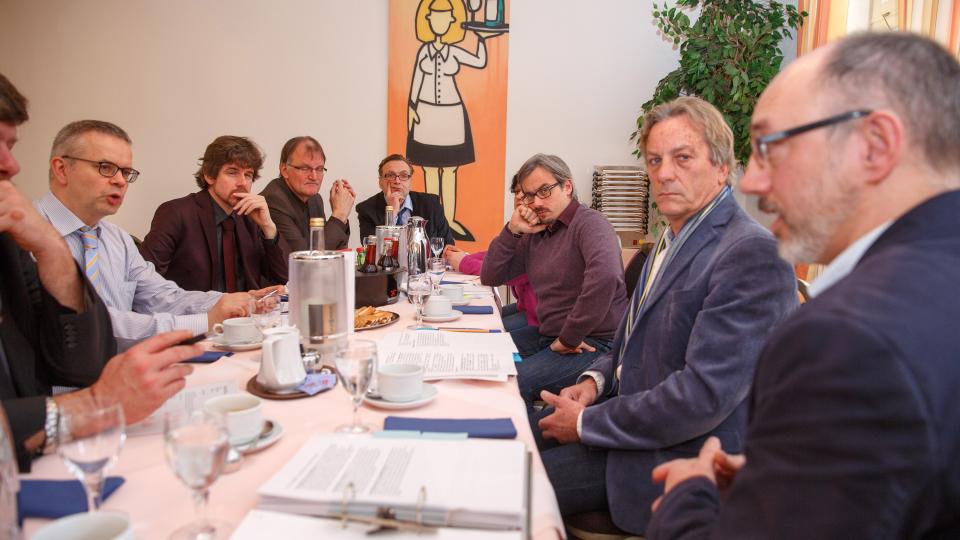 Foto: Acht Männer sitzen am Tisch und diskutieren