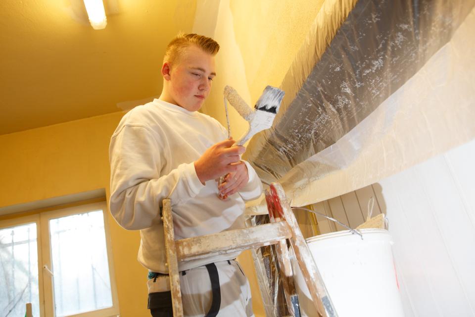 Jugendlicher Auszubildender auf Leiter mit Malerpinsel