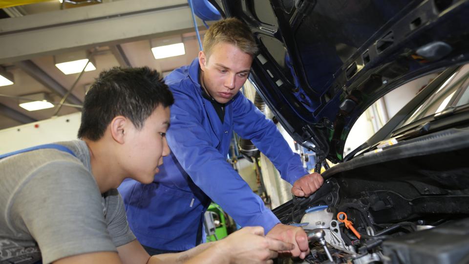 Zwei junge Auszubildende schauen in Motorraum eines Autos