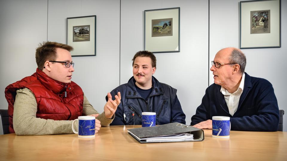 3 Männer sitzen an einem Tisch und reden