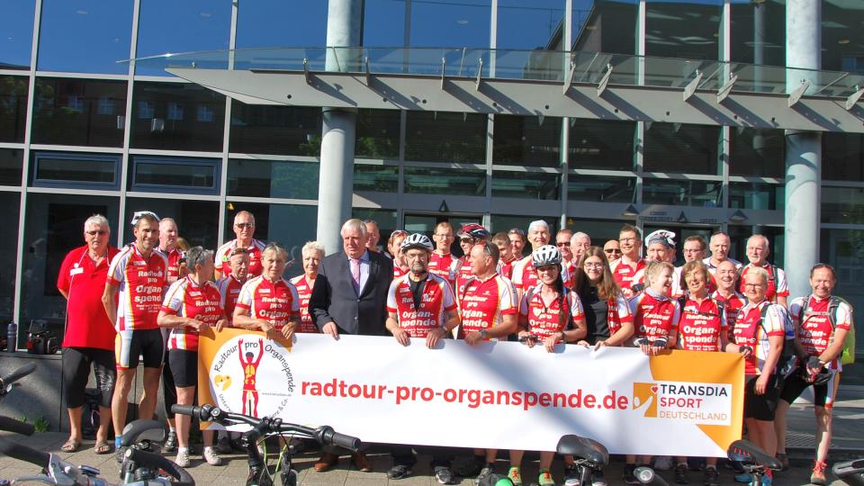 Minister Laumann steht mit den Teilnehmenden der „Radtour Pro Organspende“ vor dem Haupteingang des Ministeriums. Sie halten ein Schild mit der Aufschrift Minister Laumann mit den Teilnehmenden der „Radtour Pro Organspende“ 