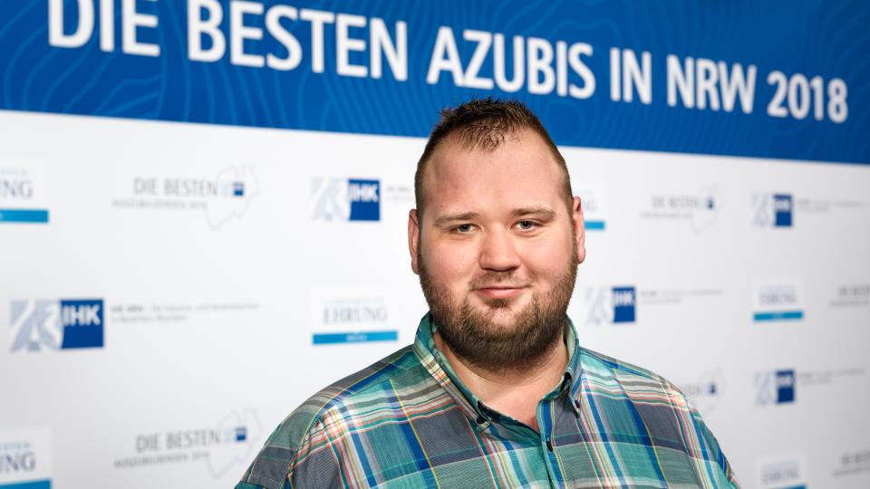 Teilnehmer mit blauem Karo-Hemd vor Banner "die besten Azubis in NRW 2018" 