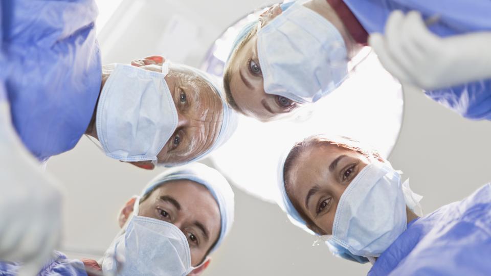 4 Ärzte mit Mundschutz beugen sich über einen Patienten