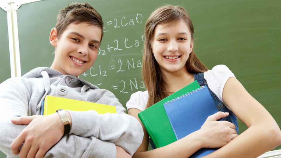 Zwei Schüler stehen lächelnd vor einer Schultafel.