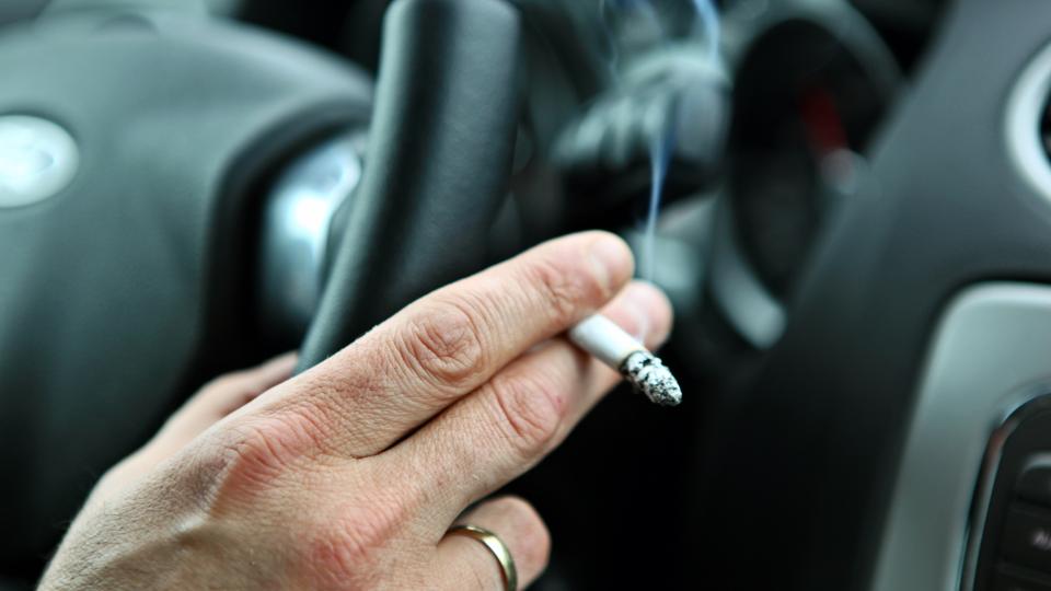 Bild zeigt die Rechte Hand eines Mannes am Steuer eines Autos. Die Hand hält eine Zigarrette.