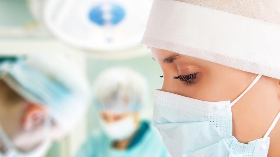 Junge Chirurgin mit zwei Ärzten im Hintergrund im Operationssaal