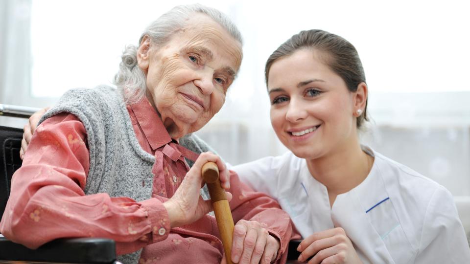 Eine Pflegerin kniet neben einer sitzenden Seniorin