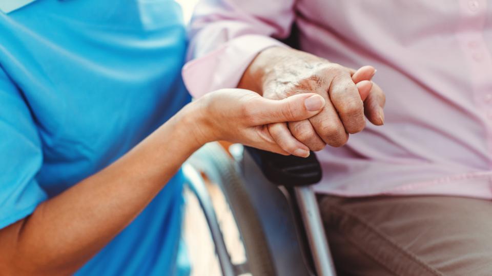 Pflegerin hält Hand halten eines Frau im Rollstuhl