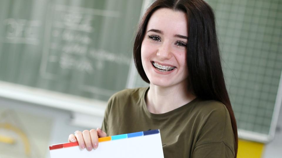 Schülerin zeigt Lernmaterial, im Hintergrund Schultafel