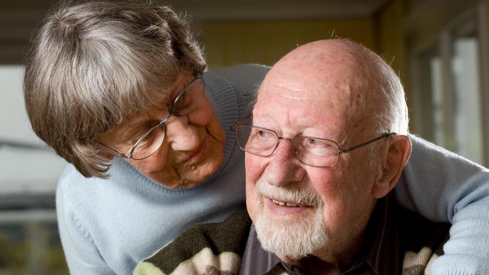 Foto zeigt eine ältere Frau mit einem Arm auf der Schulter eines älteren Mannes