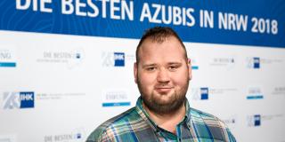 Teilnehmer mit blauem Karo-Hemd vor Banner "die besten Azubis in NRW 2018" 