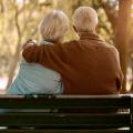 altes Paar sitz auf einer Bak und hält sich im Arm
