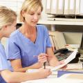 Zwei Frauen in medizinischer Arbeitskleidung sitzen an einem Schreibtisch und schauen sich ein Blatt Papier an.