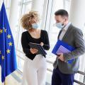 Kollegiales Gespräch zwischen einer Frau und einem Mann auf dem Flur, neben einer EU-Flagge